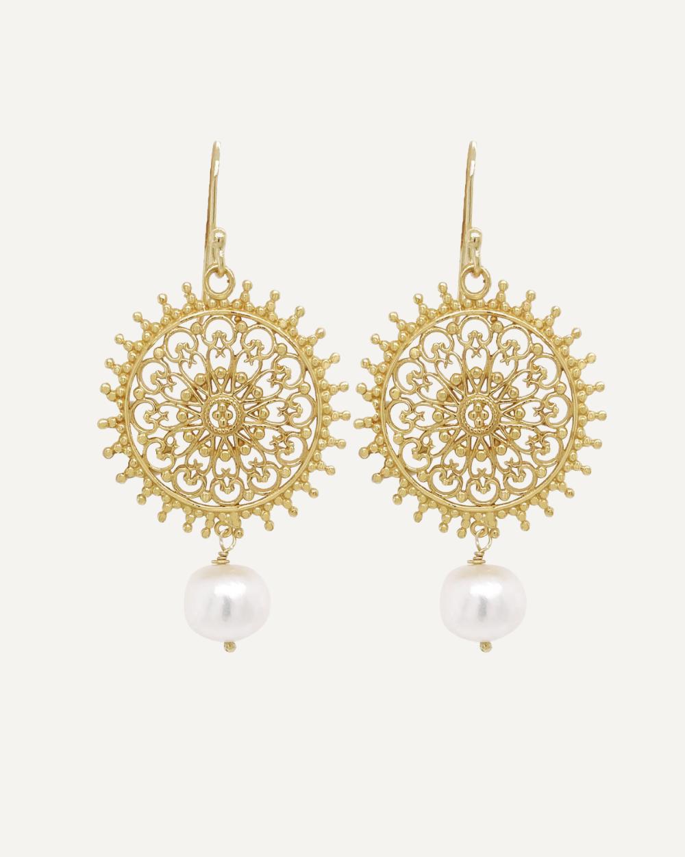 Statement earrings golden mandala shape with white baroque pearl drop on cream background.