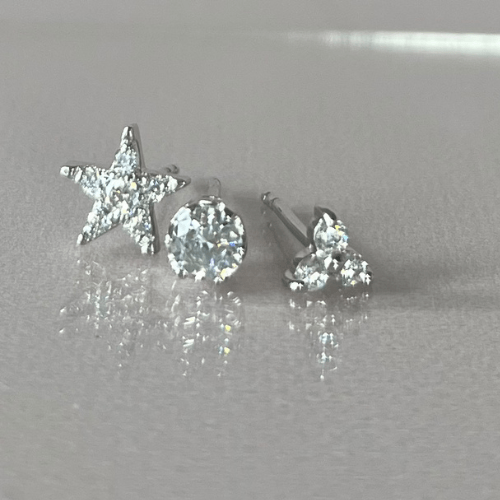 star, solitaire and trio diamond simulant stud earrings on reflective grey surface.