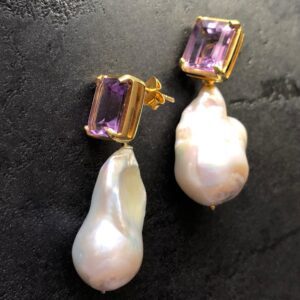 Amethyst and pearl drop earrings on grey tile background.