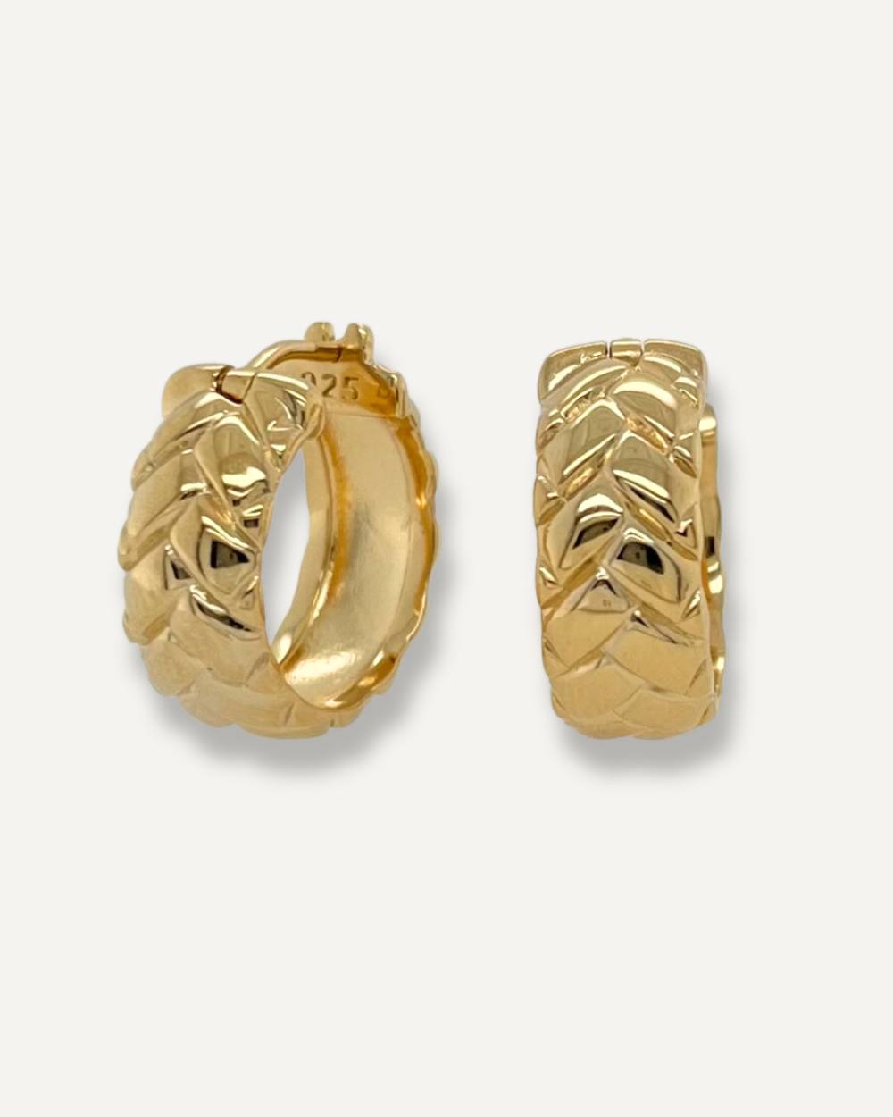 Chunky hoop earrings with surface design of tyre track in gold on cream background.